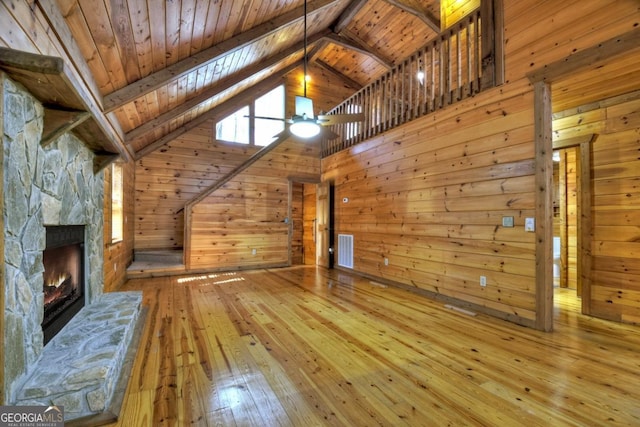 unfurnished living room with wooden ceiling, visible vents, wood walls, and a stone fireplace
