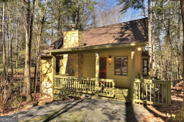 rustic home featuring a shingled roof, stone siding, and a chimney