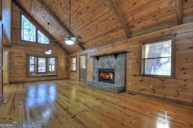 unfurnished living room with wood ceiling, wood finished floors, a stone fireplace, wood walls, and beam ceiling
