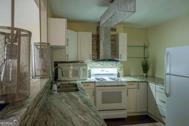 kitchen with white appliances, white cabinetry, wall chimney range hood, light stone countertops, and decorative backsplash