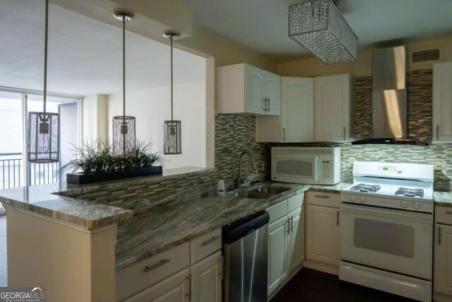 kitchen with white appliances, white cabinetry, decorative light fixtures, wall chimney range hood, and kitchen peninsula