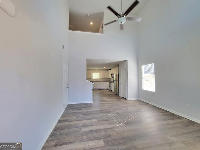 unfurnished living room with ceiling fan, light hardwood / wood-style flooring, and a towering ceiling