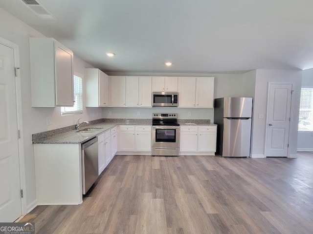 kitchen featuring sink, light stone counters, light wood-type flooring, white cabinetry, and stainless steel appliances