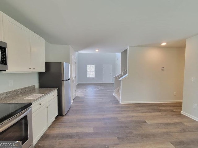 kitchen with stainless steel appliances, white cabinetry, light stone countertops, and light hardwood / wood-style flooring