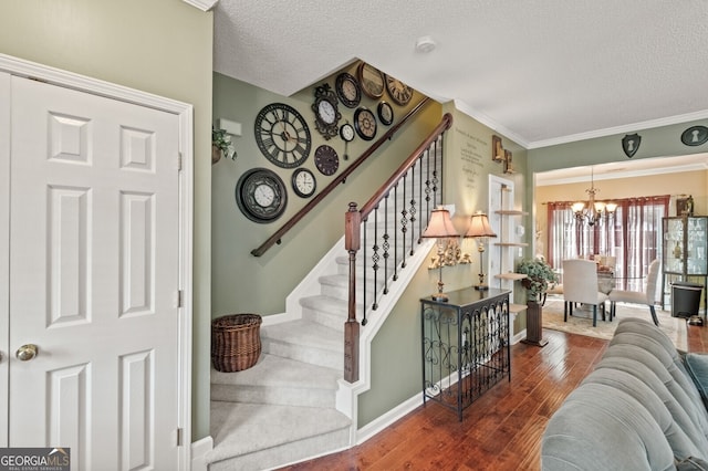 stairs with a textured ceiling, wood-type flooring, a notable chandelier, and ornamental molding