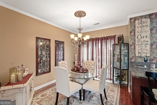 dining space with a textured ceiling, ornamental molding, hardwood / wood-style floors, and a chandelier