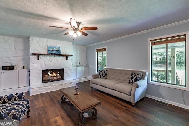 living room with a textured ceiling, dark wood-type flooring, ornamental molding, and a fireplace