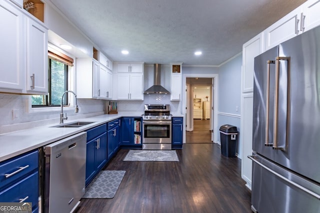 kitchen featuring appliances with stainless steel finishes, sink, white cabinetry, blue cabinets, and wall chimney range hood