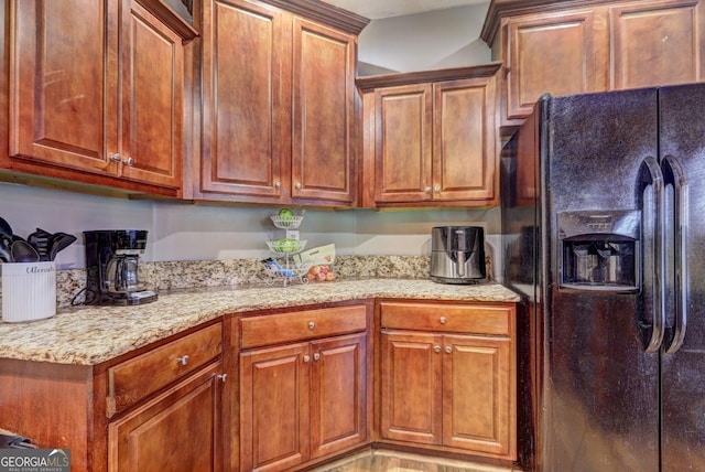 kitchen featuring light stone counters, brown cabinets, and black fridge