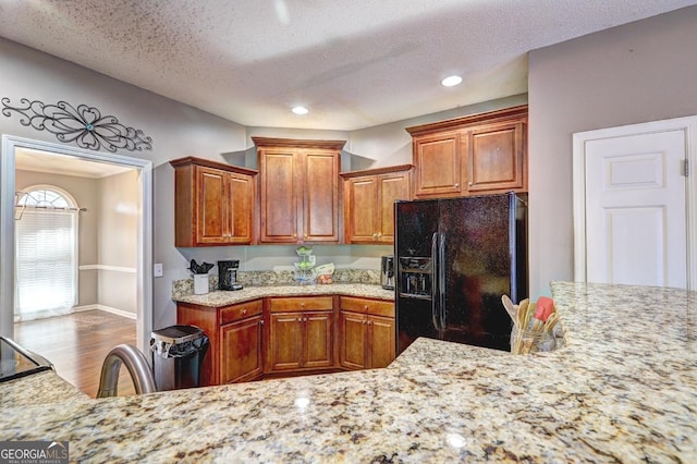 kitchen featuring brown cabinets, a textured ceiling, black refrigerator with ice dispenser, and wood finished floors