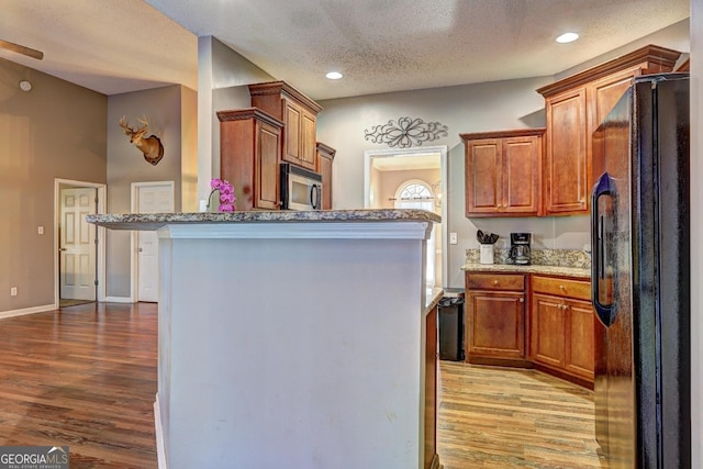 kitchen with a kitchen breakfast bar, light wood-style floors, freestanding refrigerator, brown cabinets, and stainless steel microwave