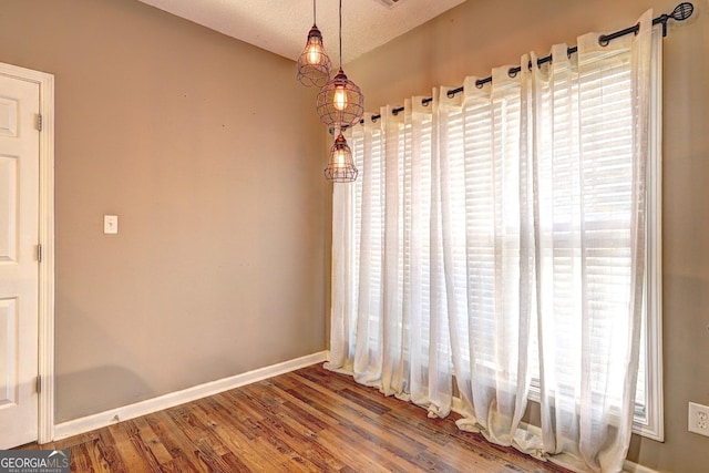 spare room featuring a textured ceiling, baseboards, and wood finished floors