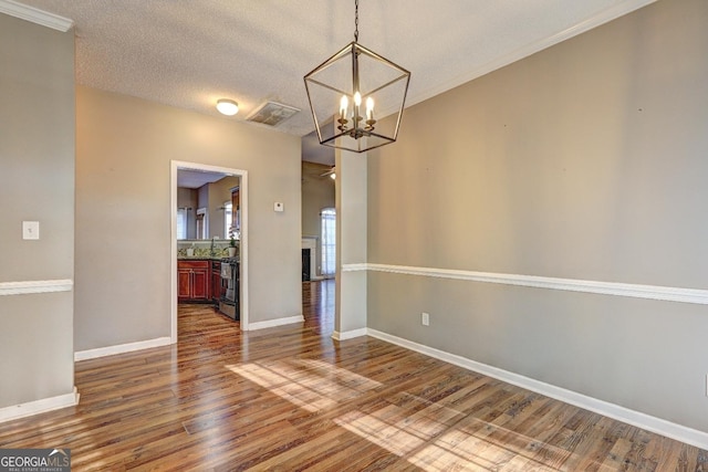 unfurnished dining area featuring baseboards, a textured ceiling, an inviting chandelier, and wood finished floors