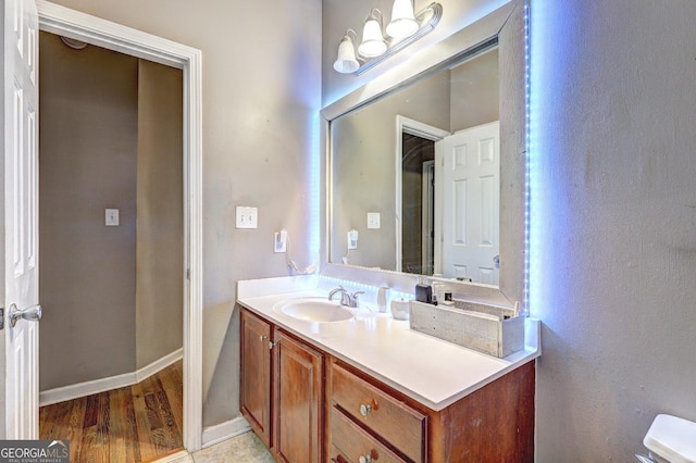 half bath with toilet, baseboards, wood finished floors, and vanity