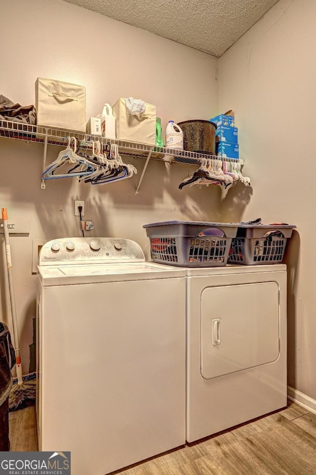 laundry area with laundry area, light wood finished floors, baseboards, washer and clothes dryer, and a textured ceiling