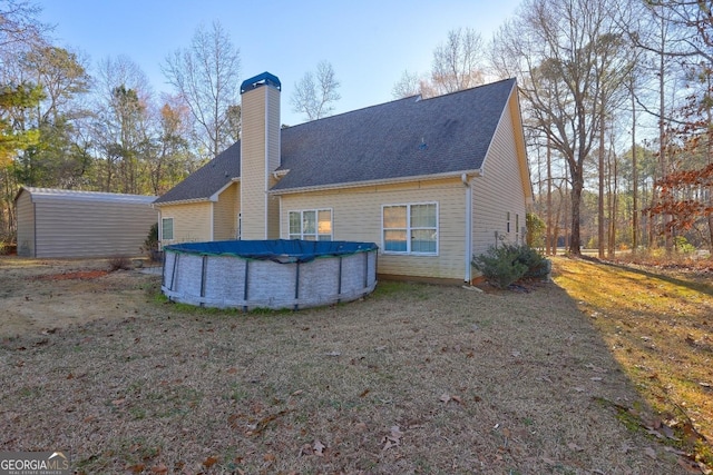 back of property with a shingled roof, a chimney, and a covered pool