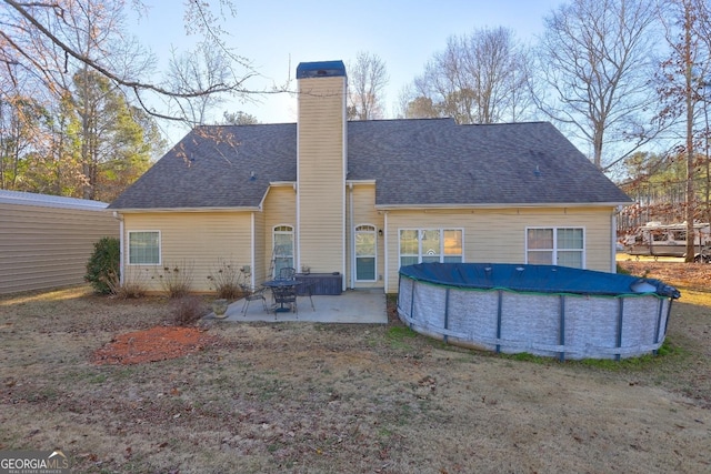 rear view of house with a covered pool, a chimney, a shingled roof, and a patio