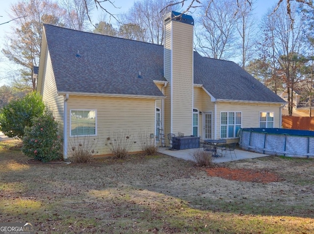 rear view of house featuring a patio, a shingled roof, a chimney, and a covered pool