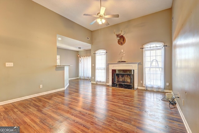 unfurnished living room featuring ceiling fan, a premium fireplace, wood finished floors, and baseboards