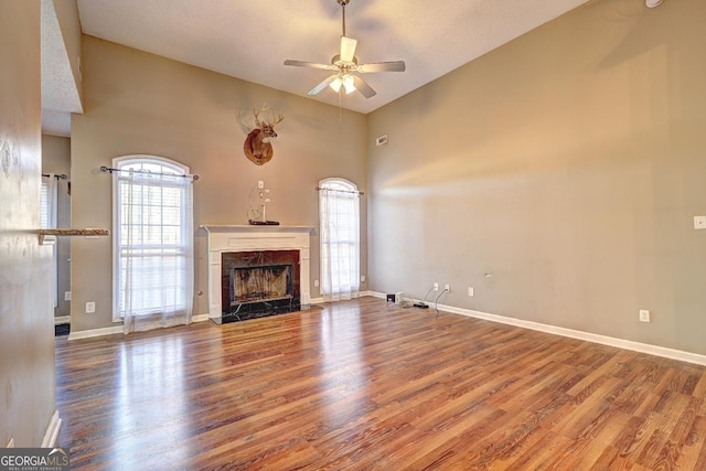 unfurnished living room featuring a fireplace, a high ceiling, a ceiling fan, wood finished floors, and baseboards