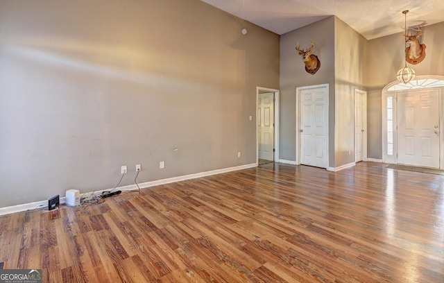 interior space featuring dark wood-style flooring, a towering ceiling, and baseboards