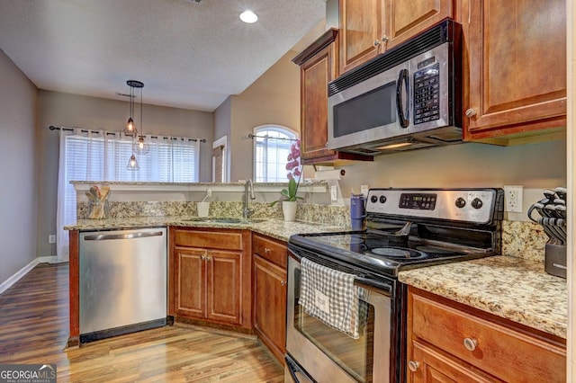 kitchen with stainless steel appliances, brown cabinets, a sink, and light wood finished floors