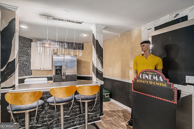 kitchen with light hardwood / wood-style flooring, pendant lighting, stainless steel fridge with ice dispenser, white cabinets, and a breakfast bar area