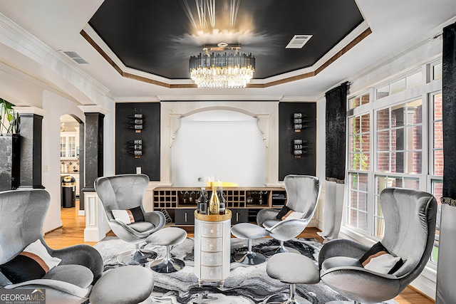 living area with a tray ceiling, light hardwood / wood-style floors, crown molding, and ornate columns