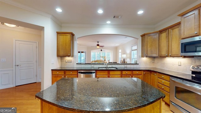 kitchen with light wood-type flooring, a center island, sink, tasteful backsplash, and appliances with stainless steel finishes