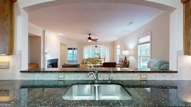 kitchen featuring a fireplace, sink, tasteful backsplash, dark stone counters, and crown molding