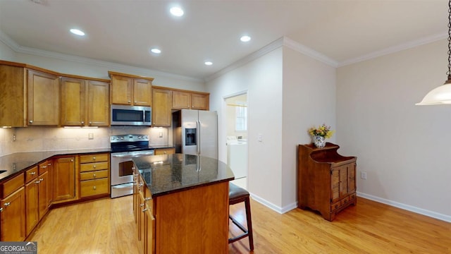 kitchen with appliances with stainless steel finishes, hanging light fixtures, decorative backsplash, a kitchen island, and light wood-type flooring