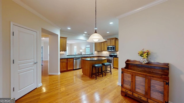 kitchen with a breakfast bar, light wood-type flooring, stainless steel appliances, crown molding, and hanging light fixtures