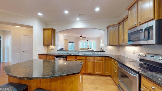 kitchen with stainless steel appliances, light hardwood / wood-style flooring, a kitchen island, sink, and dark stone counters