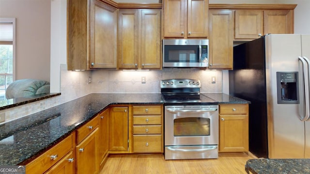 kitchen with dark stone countertops, light hardwood / wood-style flooring, stainless steel appliances, and decorative backsplash