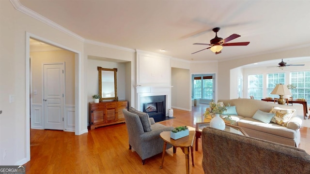 living room with ceiling fan, ornamental molding, light wood-type flooring, and a wealth of natural light