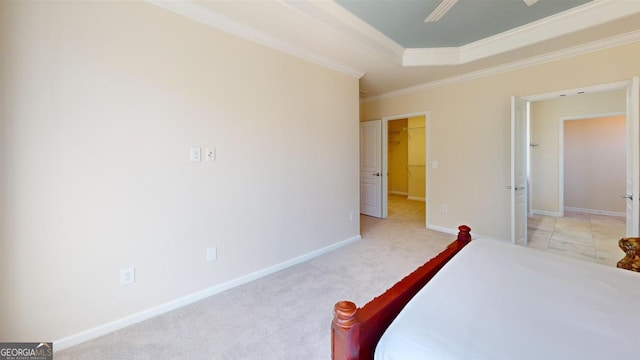 unfurnished bedroom with light carpet, a tray ceiling, a spacious closet, and ornamental molding