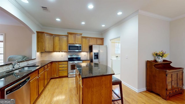 kitchen featuring stainless steel appliances, a center island, dark stone countertops, washer / dryer, and a breakfast bar area