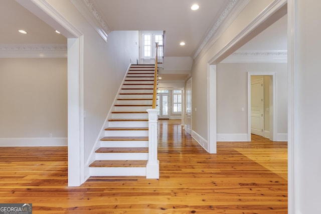 stairs with wood-type flooring, a wealth of natural light, and crown molding