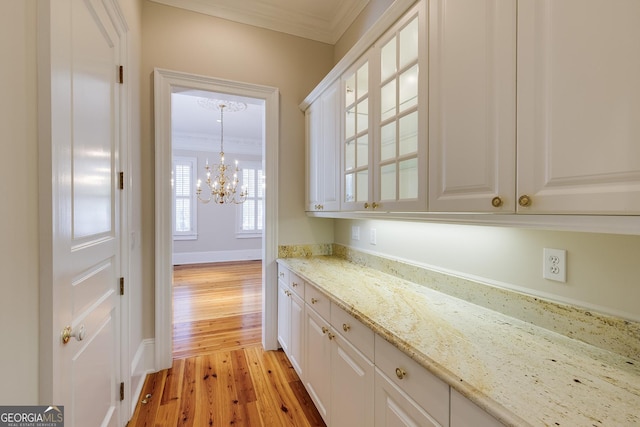 interior space with light hardwood / wood-style flooring, light stone countertops, ornamental molding, white cabinets, and a chandelier