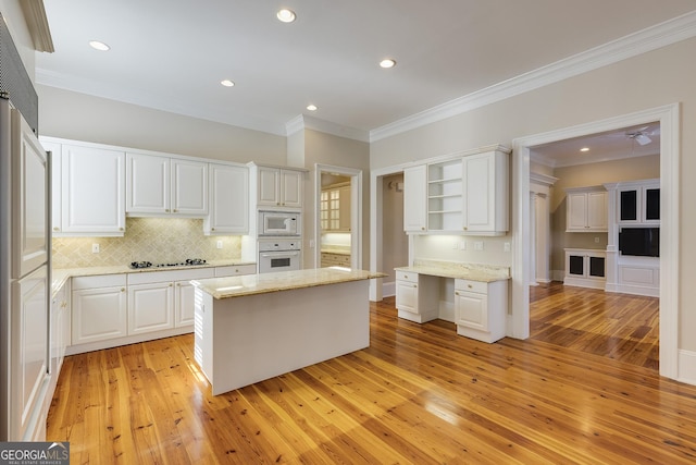 kitchen with white appliances, light wood-type flooring, white cabinetry, a kitchen island, and light stone countertops