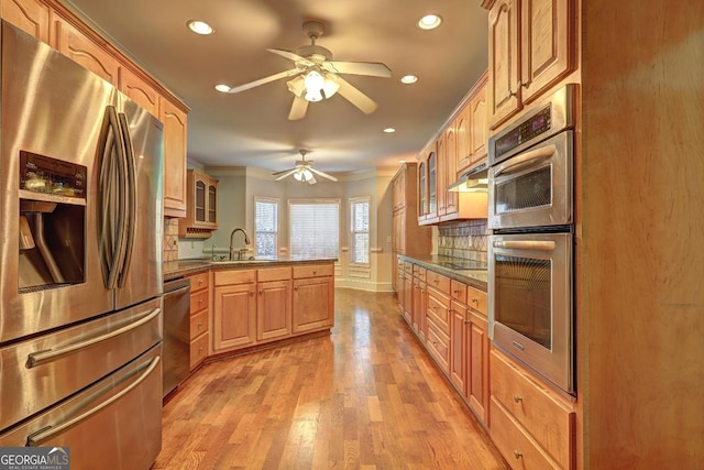 kitchen with stainless steel appliances, tasteful backsplash, glass insert cabinets, a sink, and light wood-type flooring