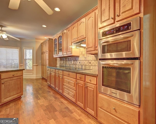 kitchen with ceiling fan, double oven, black electric cooktop, under cabinet range hood, and glass insert cabinets