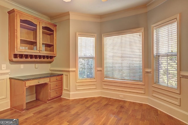 unfurnished office featuring light wood-type flooring, crown molding, built in desk, and wainscoting