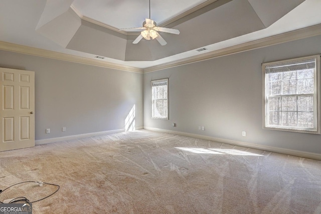 spare room with a tray ceiling, light carpet, crown molding, and baseboards