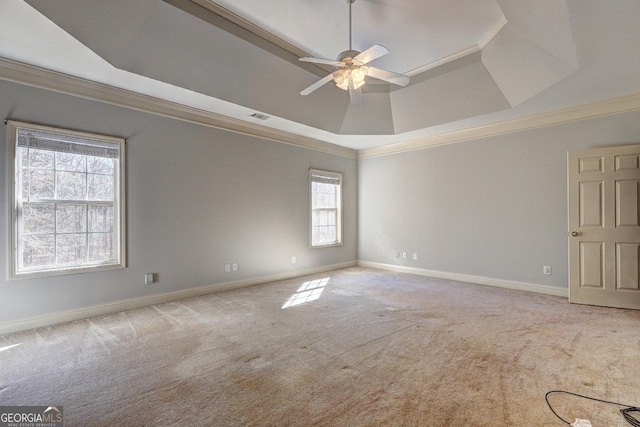 empty room with light carpet, visible vents, a raised ceiling, baseboards, and ornamental molding