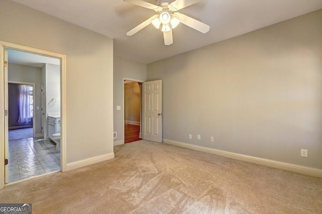 unfurnished bedroom featuring light carpet, ensuite bath, baseboards, and ceiling fan