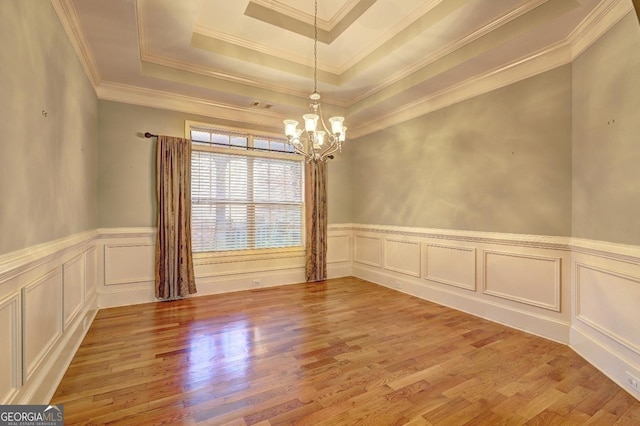 unfurnished room featuring light wood finished floors, a raised ceiling, wainscoting, ornamental molding, and a chandelier