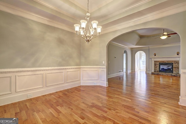 interior space with a tray ceiling, arched walkways, a fireplace, light wood-style flooring, and ceiling fan with notable chandelier