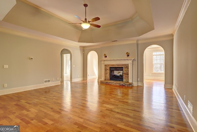 unfurnished living room with light wood-style floors, a tray ceiling, crown molding, and a stone fireplace