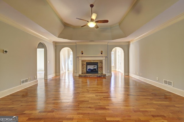 unfurnished living room featuring visible vents, ornamental molding, light wood-type flooring, a brick fireplace, and a raised ceiling